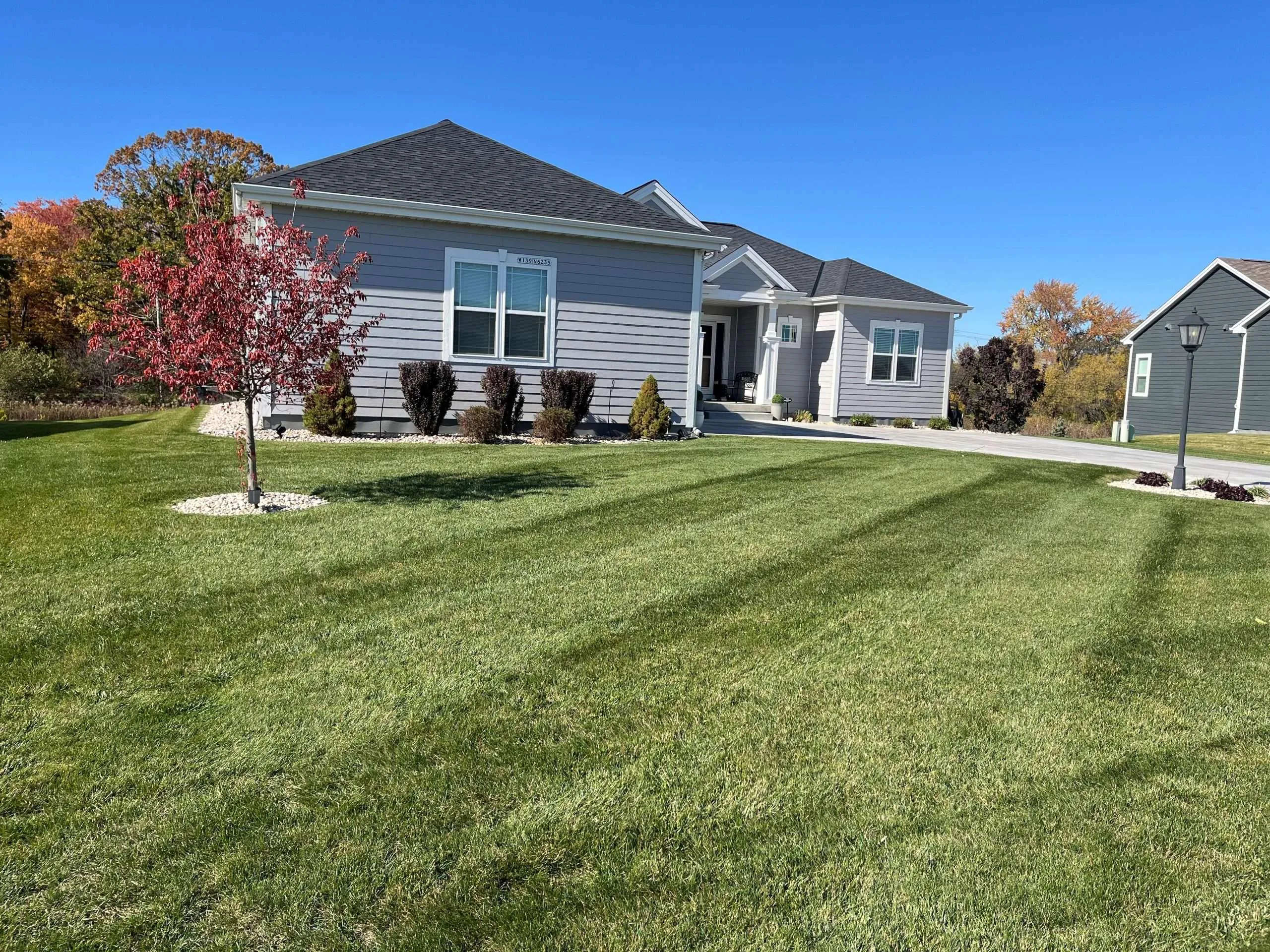 Uniform lawn stripes stretching across the front of a ranch-style home with autumn landscaping accents.