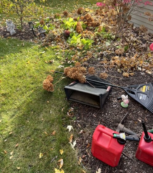 Rakes and collection bags staged for autumn garden cleanup near flower beds, ready for leaf removal.