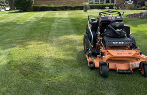 lawn-mower-done-striping-landscape A large black and orange lawn mower in the foreground after completing lawn mowing and lawn striping services.