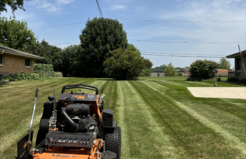 Portrait shot of a large orange and black lawn mower in the foreground after completing lawn mowing and striping service.