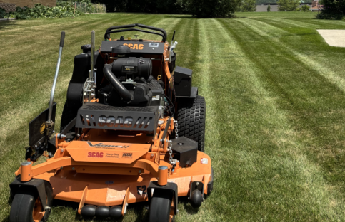 lawn-mower-finished-stripping-portrait Portrait shot of a large orange and black lawn mower in the foreground after completing lawn mowing and striping service.