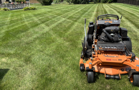 lawn-mower-finished-cross-striping Landscape shot of a patio, back yard, and a large orange lawn mower in the foreground after lawn mowing and lawn stripping service.