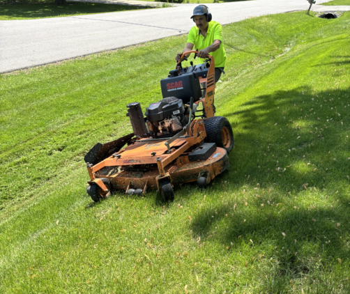 lawn-striping-with-team A&M team leader mowing a front lawn next to a suburban curb.